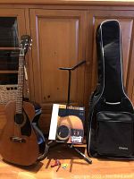 Full view of vintage Regent acoustic guitar next to tripod guitar stand, soft case, method book, picks and capo on floor