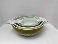 Full set of four vintage Pyrex nesting mixing bowls arranged inside each other, showing avocado green exterior with white interior.