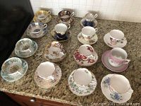 Overview of all 15 bone china teacup and saucer sets arranged on countertop