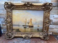 Full front view of painting and ornate gilt frame leaning against stone backdrop
