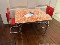 Overall view of small American Girl Molly table with orange marbled plastic top and two red chairs with chrome frames.