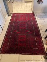 Full view of red Persian Baluchi area rug laid on tile floor