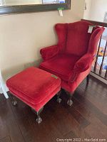 Full view of the red upholstered wingback armchair and matching ottoman set, showing size, color, and shape.