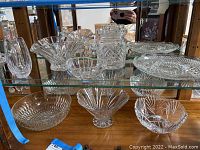 Various crystal and glass bowls, platter and ice bucket on glass shelf in wooden display cabinet.