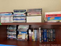 Shelf holding a large number of DVDs and VHS tapes, showing rows with various titles stacked.