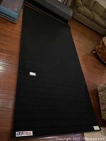 Full view of EZ Flex sports mat rolled out on wooden floor showing black textured surface and EZ Flex logo in corner.
