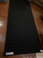 Full view of the large black exercise mat laid flat on a wooden floor showing size and texture.