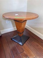 Side view of the round wooden side table with tapered pedestal and black metal base on wooden floor.