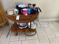 Full view of Italian wood inlaid serving cart with multiple cups, plates, and bowls on top and below tiers.