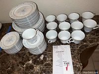 Complete Noritake Carolyn tableware service for 12 showing stacked plates and cups on a marble countertop.