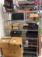 Full view of 6-tier metal rolling storage shelf with boxes and miscellaneous items on and around it.