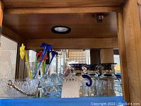 Shelf with assorted clear glass bowls, swan figurines, and colorful glass flower stems.