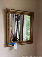 Full view of the square gold-framed wall mirror hung on a wall.