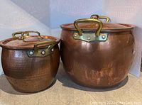 Two copper pots side by side with lids