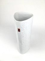 Front angle showing the white porcelain vase with embossed floral patterns and a red and gold label on the side.