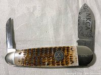 The pocket knife's handle and blades fully extended showing engraved NKCA 1989 on large blade and serial number 2292 on bolster.