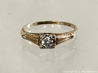 Front view showing single round diamond set in four‐prong white gold head with engraved yellow gold shoulders