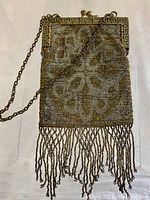 Front view of a small silver and gold beaded antique purse with an ornate metal frame and chain handle, showing detailed beadwork pattern and fringe.
