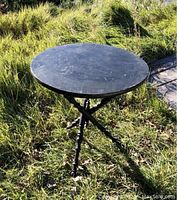 Full view of round black wooden table with three spindle-turned legs in gothic style on grass outdoors.