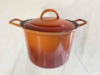 Front and side view of deep orange enamel cast iron stock pot with lid attached showing overall condition.