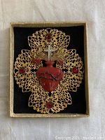 Front view of large Sacred Heart pin in original box showing detailed red heart with crown of thorns, gold flames, silver cross, and filigree backing with red gemstone accents.