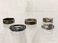 Five sterling silver rings laid out in a row showing front designs and band widths.