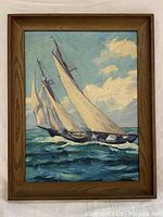 Framed oil painting showing a sailboat on the ocean with big sails and partly cloudy sky.