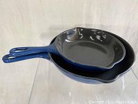 Two stacked blue enamel cast iron skillets with black interior, viewed from side showing handles and rims