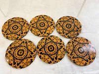 Top view of six identical round metal coasters laid out on a white surface showing the orange and black psychedelic pattern.