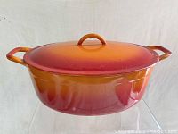 Side view of the oval Dutch oven showing orange to red ombre enamel and handles.