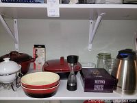 Overview of the lot items on white shelf including casseroles, warming dish, jars, Thermos carafe, and Brie baker box.