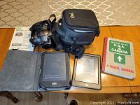 Photo showing Canon camera with case and two Kobo e-readers on table along with a travel journal.