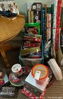 Wide view of Christmas wrapping supplies, gift bags, and holiday tins displayed on floor and table.