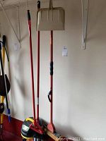 Photo showing red handled dustpan, broom, brush, and Stanley vacuum in corner