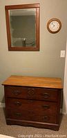 Photo of a vintage wooden dresser with three drawers underneath a wood framed beveled mirror and a wood framed wall clock.