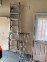 Overview of aluminum extension ladder and two adjustable crutches leaning against wall in garage.