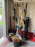 Wide view of gardening tools standing in corner including rakes, shovels, and tomato stands.