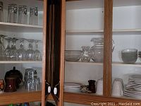 Two cupboards with glassware and dinnerware including plates, bowls, cups, teapot, mugs, glass pitchers, and glasses.