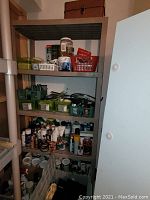 A metal shelving unit with multiple plastic bins containing small hardware items such as screws and brackets, bottles of chemicals and cleaners, and a metal toolbox on the bottom shelf.