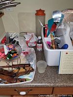 Countertop with plastic tray, kitchen tools including spatulas, scissors, pizza wheel, batting brush, plastic clips, container with red lid, and miscellaneous small items.