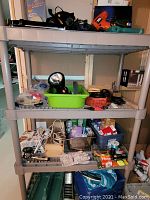 Full view of shelving unit with multiple power tools, spotlight, gardening gloves, and various hardware items on three shelves.
