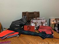 Collection of various purses, bags, belt, and umbrella arranged on wooden table