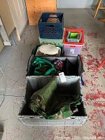 Photo showing variety of storage bins stacked including milk crates, pink small bin, and large gray bin with camouflage tarp and bags inside