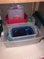 Plastic storage totes stacked in basement corner including clear and blue totes with lids.
