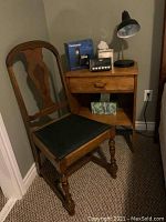 Photo of the vintage splat back wooden chair, night table holding lamp, clock radio, tissue box, and boxed cordless phone, positioned in a corner near carpeted floor.