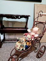 Wooden book/magazine table and vintage doll pram with three rag dolls displayed on pram seat