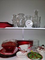 Shelf containing felt red placemats, multiple clear glass vases of varying shapes and sizes, and a small white clock. Bottom area includes assorted red and clear glass dishes, Christmas themed items, and glass trays.