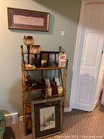 Full view of wooden ladder shelf with multiple candles, candle holders, card games, framed sailboat painting leaning in front