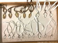 Overall view of 15 small Swarovski crystal Christmas ornaments including amber leaf shapes with brown ribbons labeled 2014 and 2015, and clear cross shapes with white ribbons.