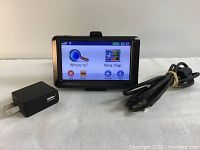 Garmin nuvi GPS navigator with screen on showing main menu, USB cable and wall adapter charger beside it on white background.